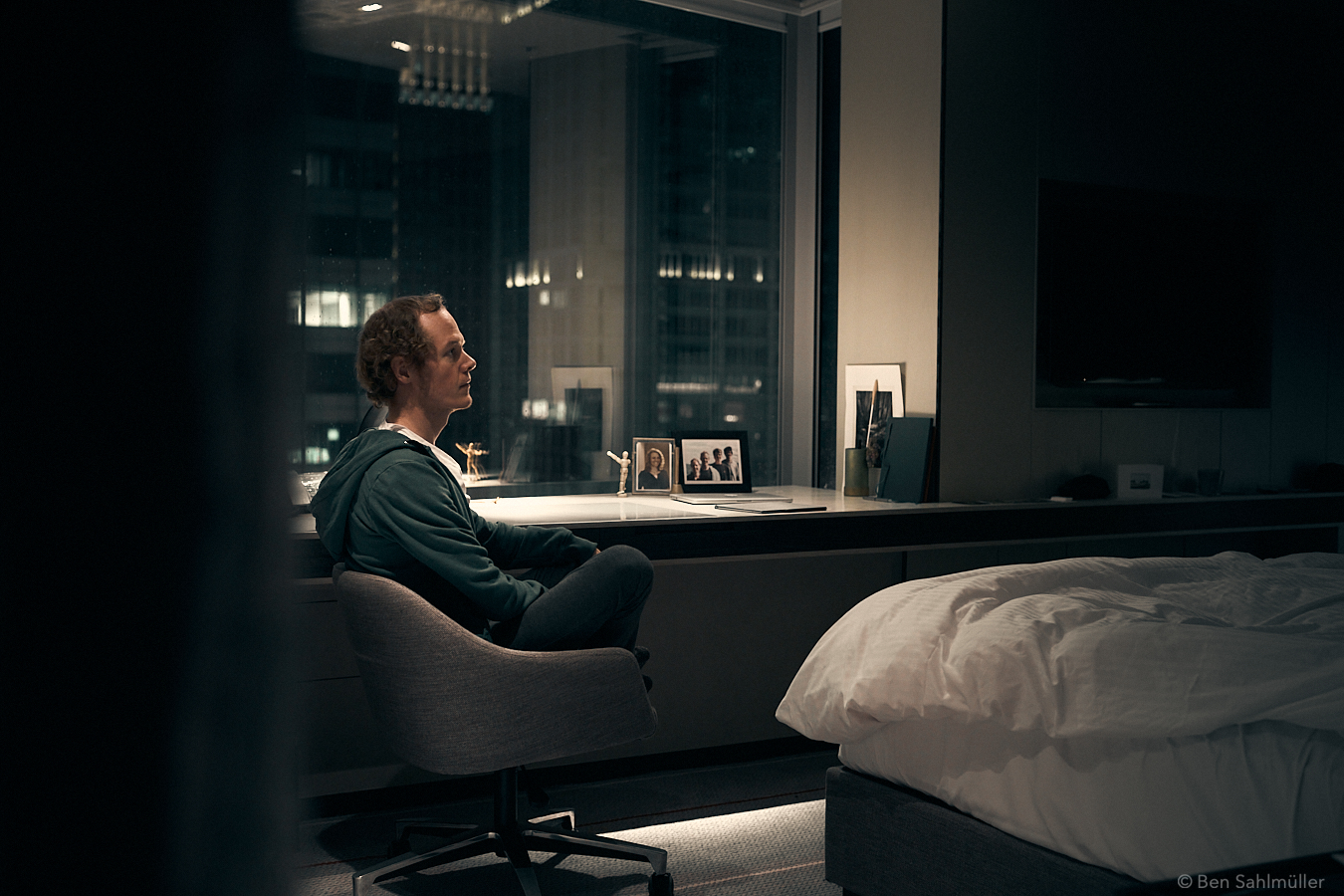 A young man sitting on a chair in a hotel room by night. He seems occupied with his thoughts, the scene reminds a bit of a film noir.