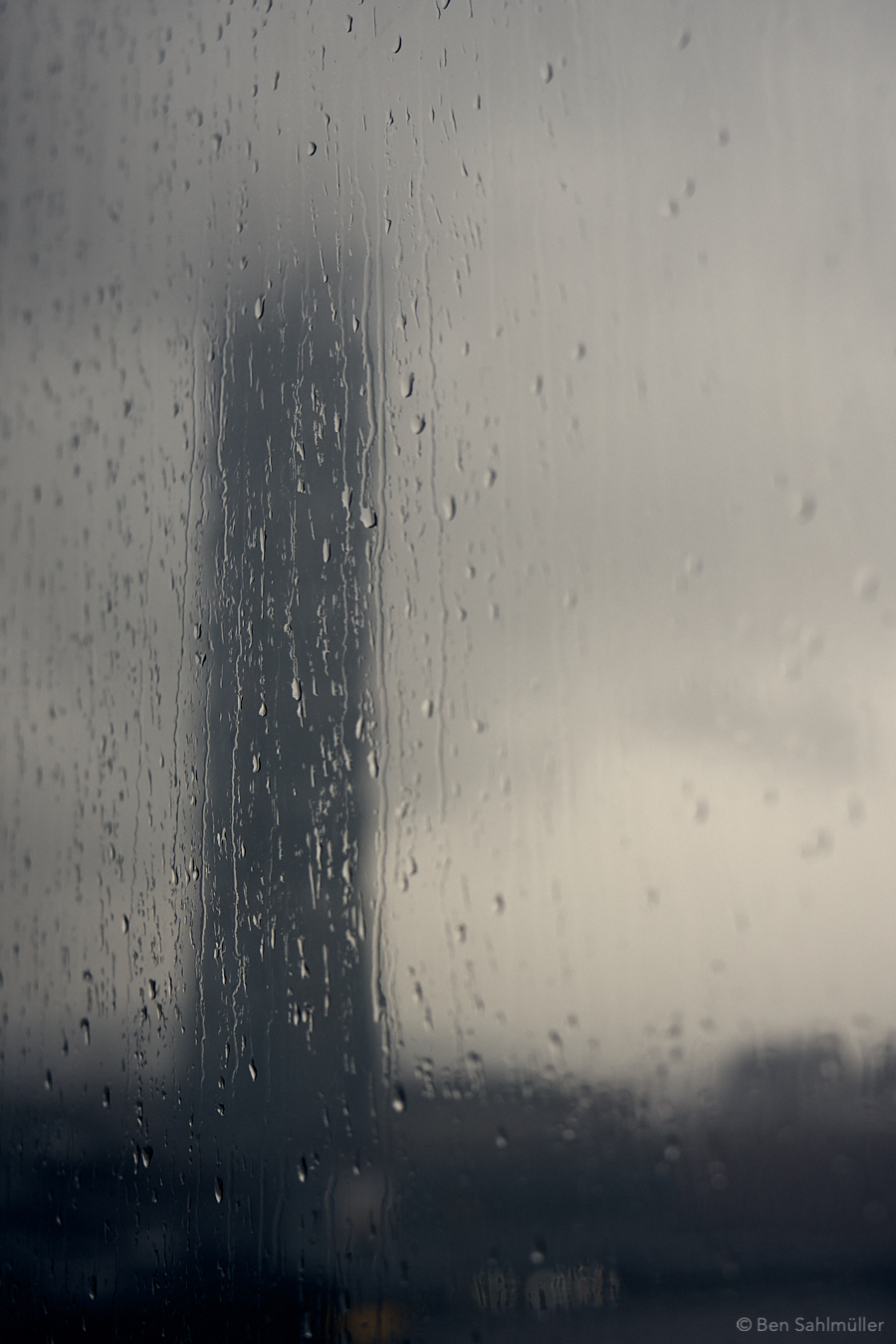 Taipei 101 as seen through a window glass. There are raindrops on the glass and the tower itself is just a dark silhouette.