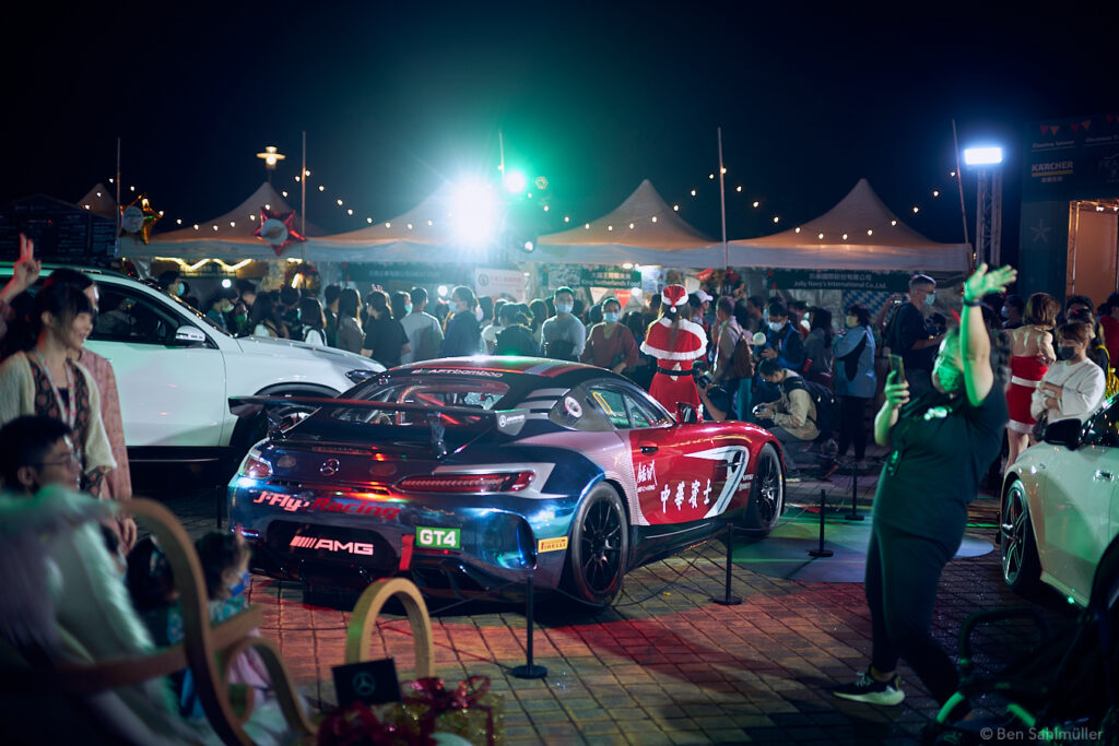 A sports car displayed at a German Christmas market in Taipei, presented by a young women in a Santa Claus costume.
