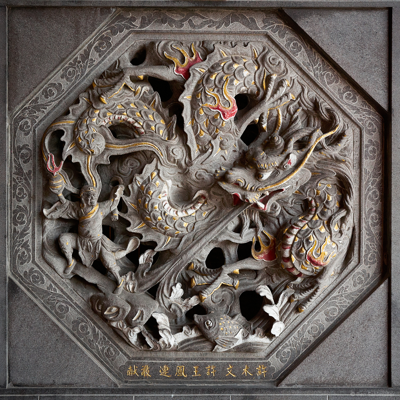 A stone sculpture in a wall. It depicts a dragon fighting against a warrior holding a grenade.