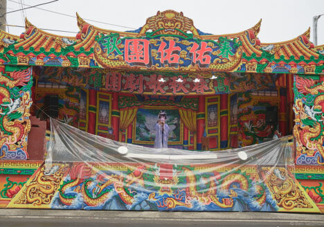 A big opera stage at a street. A sole singer in standing in its center.