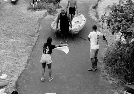 Two men carrying light plastic boats, a woman standing before them waving a towel like a matador.