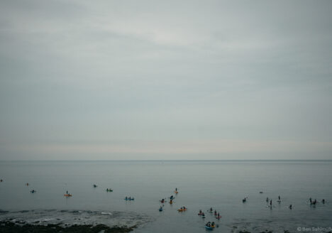 The sea, calm as a pancake. People are doing stand up paddling or paddling smaller boats. There are scooters and small trucks standing at the shore to bring them back later.