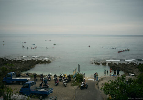 The sea, calm as a pancake. People are doing stand up paddling or paddling smaller boats. There are scooters and small trucks standing at the shore to bring them back later.