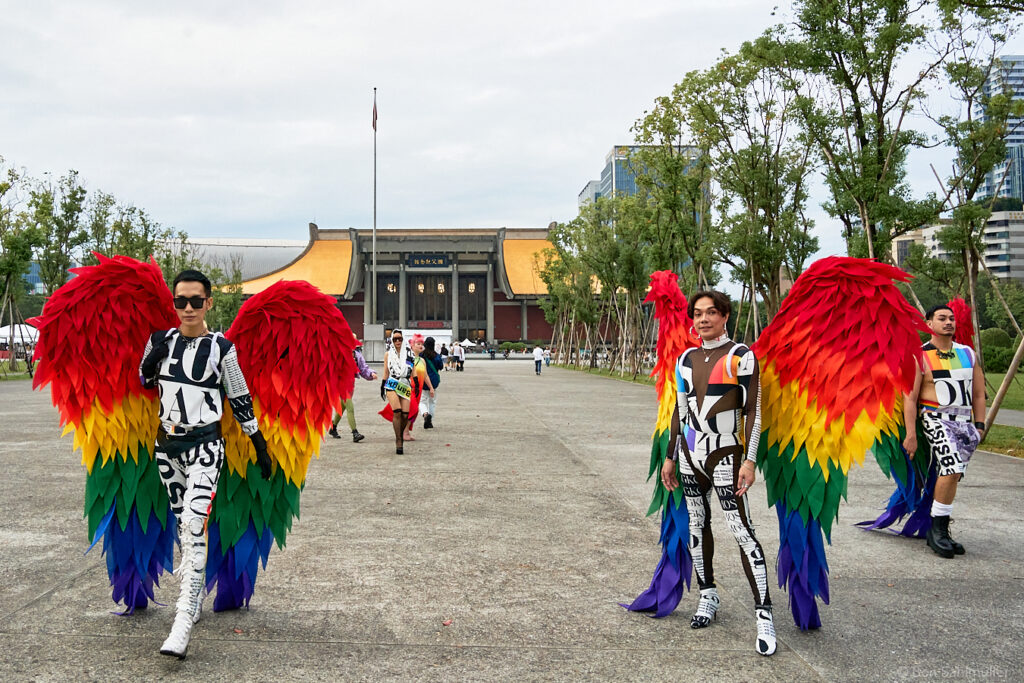 Two people dressed as angels with big rainbow-colored wings standing in front of Sun Yat-Sen Memorial. Two more angels are a bit further in the back.