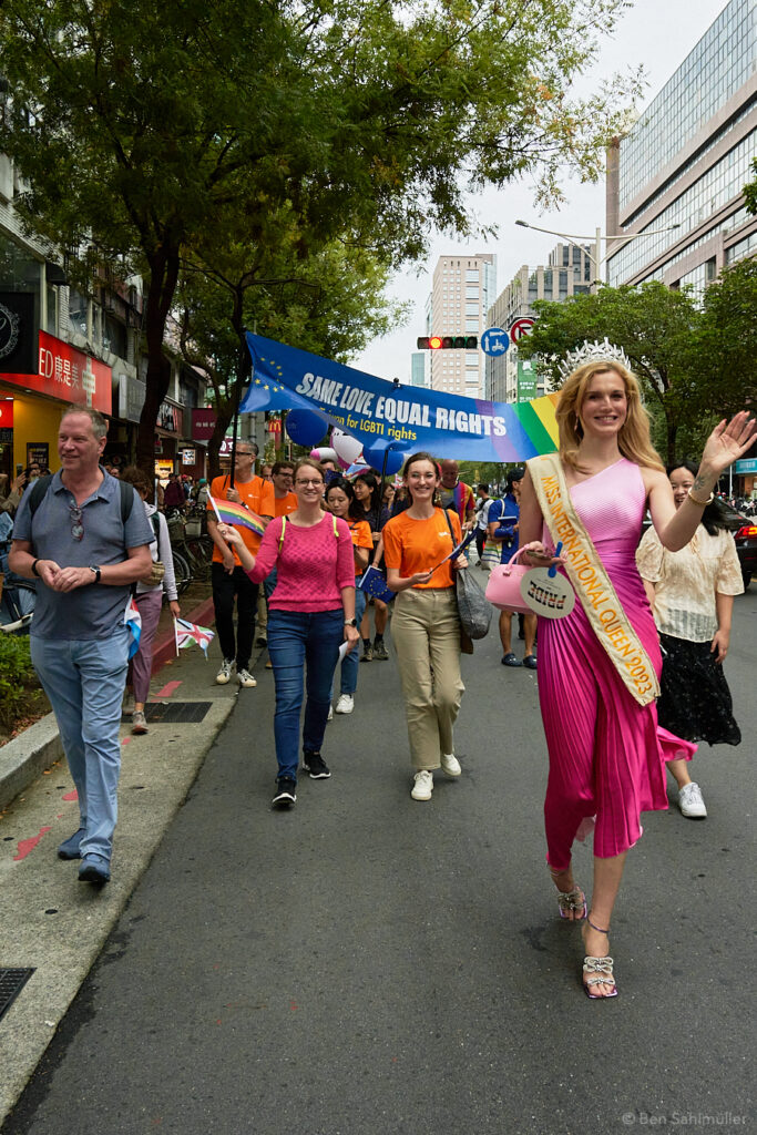Solange Dekker, a tall blonde woman wearing a pink dress, walks in front of the EU's Taiwan Pride banner. The banner reads "Same Love, Equal Rights."