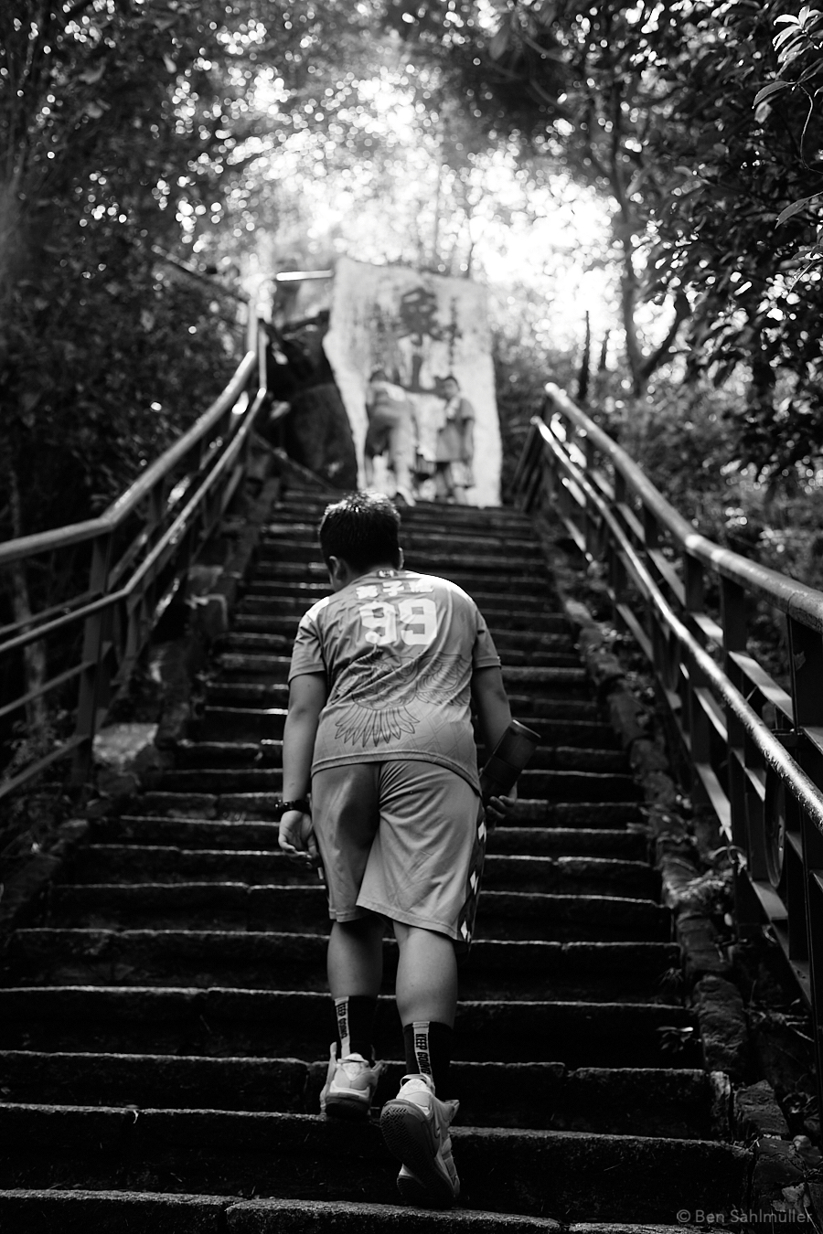 An exhausted boy stepping up the stairs towards Elephant Mountain, his friends in the background waiting for him.
